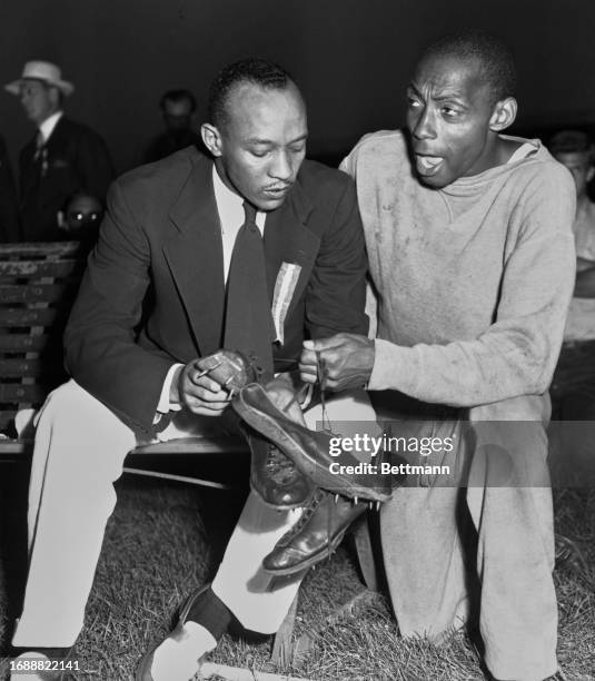 American athlete Barney Ewell holds two pairs of running shoes as he speaks with Jesse Owens at the finals of the Olympic trials in Evanston,...