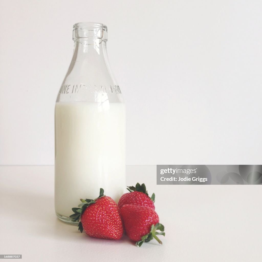 Fresh strawberries next to a glass bottle of milk