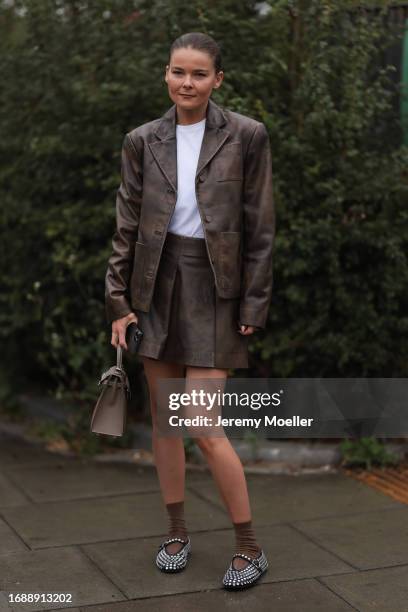 Fashion Week Guest was seen wearing a white top and a brown leather skirt and jacket, brown socks, and a brown Hermey Kelly bag as well as alaia...