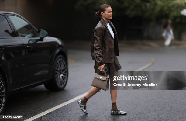 Fashion Week Guest was seen wearing a white top and a brown leather skirt and jacket, brown socks, and a brown Hermey Kelly bag as well as alaia...