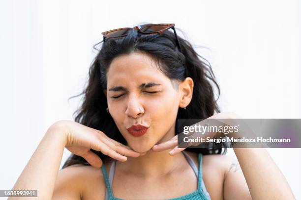 young latino woman picking up, closing her eyes, and throwing a kiss at the camera with her hands below her chin - mano sul mento foto e immagini stock