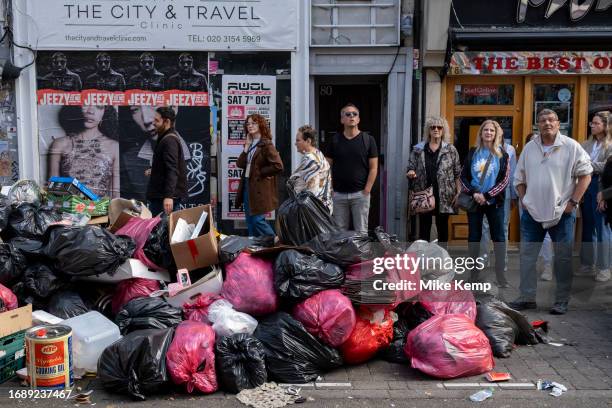 Tourists on a street art walking tour pass refuse piled up along Brick Lane during four weeks of strike action by waste service workers in Tower...