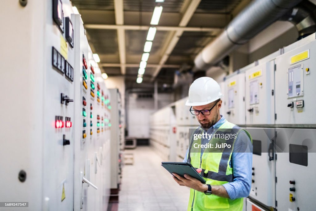 Electrical engineer checking power at control room using digital tablet