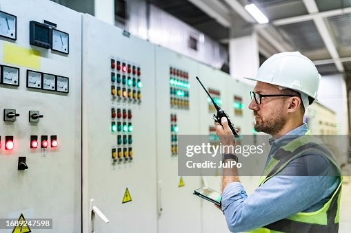 Electrical engineer checking power at control room using digital tablet and walkie-talkie Electrical engineer checking power at control room using digital tablet and walkie-talkie