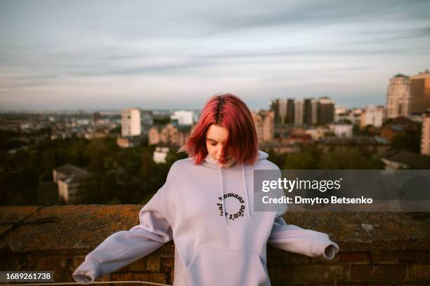 portrait of peaceful young woman standing on the rooftop of building in the city - dyed red hair 個照片及圖片檔