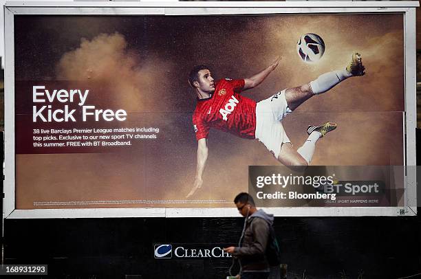 Pedestrian uses an personal electronic device as he passes a billboard advertisement for BT Group Plc's new sports television service BT Sport in...