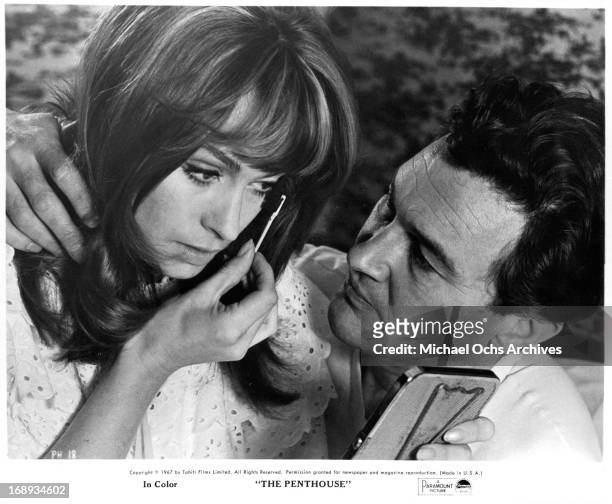 Suzy Kendall is putting on makeup while Terence Morgan watches in a scene from the film 'The Penthouse', 1967.