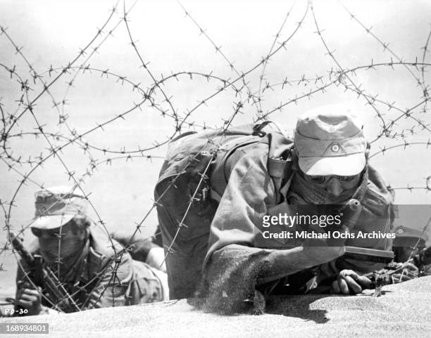 Men on active military duty scrawling on the ground looking through barbed wire at the enemy in a scene from the film 'Play Dirty', 1969.