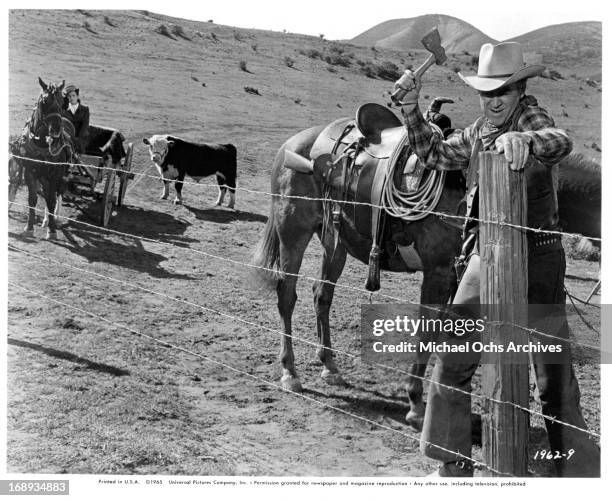 Maureen O'Hara watches James Stewart chop through barbed wire blocking their way to Texas in a scene from the film 'The Rare Breed', 1966.