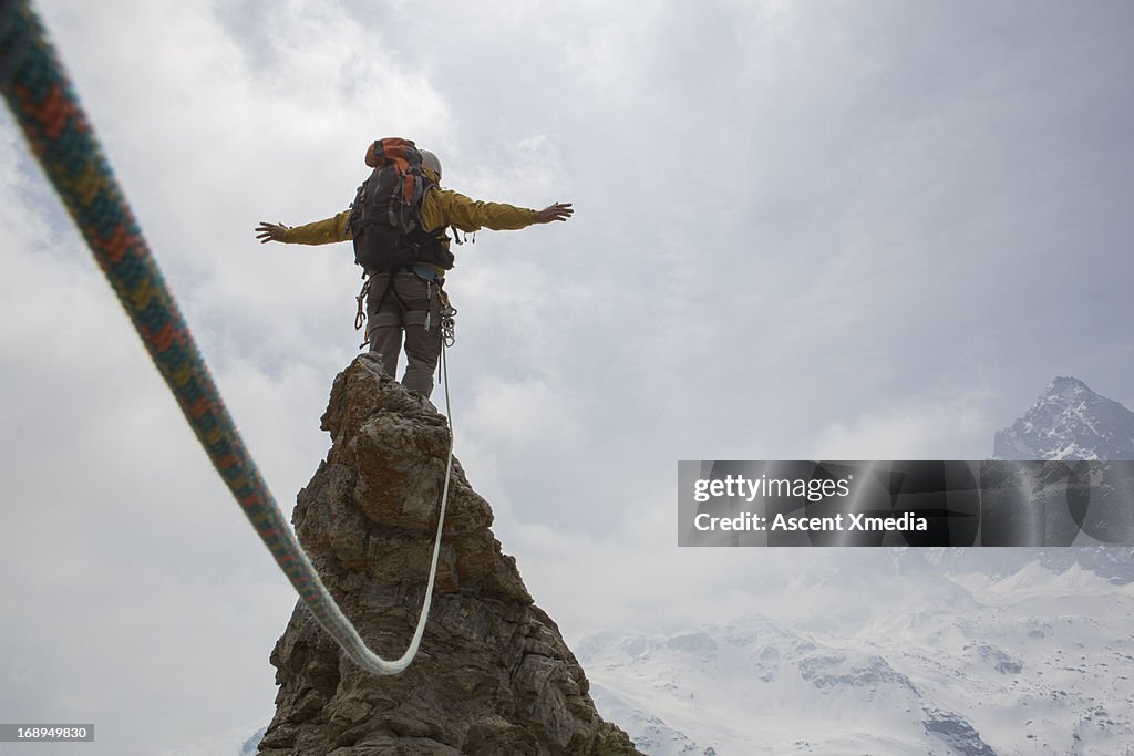 Mountaineer stands on summit, arms outstretched