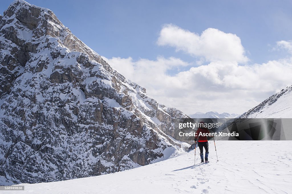 Hiker stands on snowy path, looks ahead, mtns
