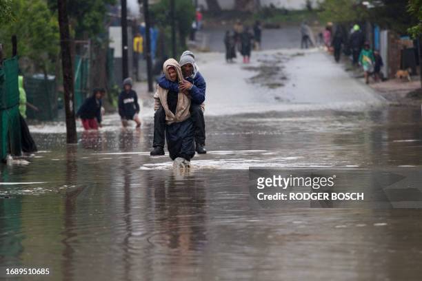 Man carries an elderly man across a flooded road during heavy flooding as a result of a storm in Sir Lowry's Village, close Somerset West on...