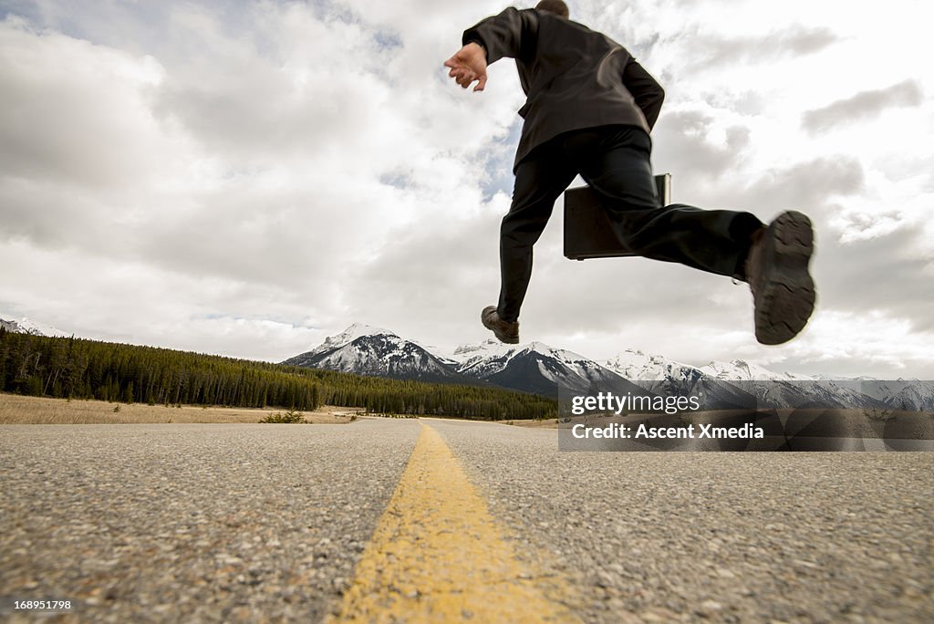 Businessman in mid-air stride above mtn road