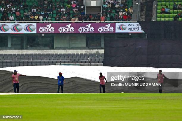 Members of ground staff cover the field as it rains before the start of the third and final one-day international cricket match between Bangladesh...