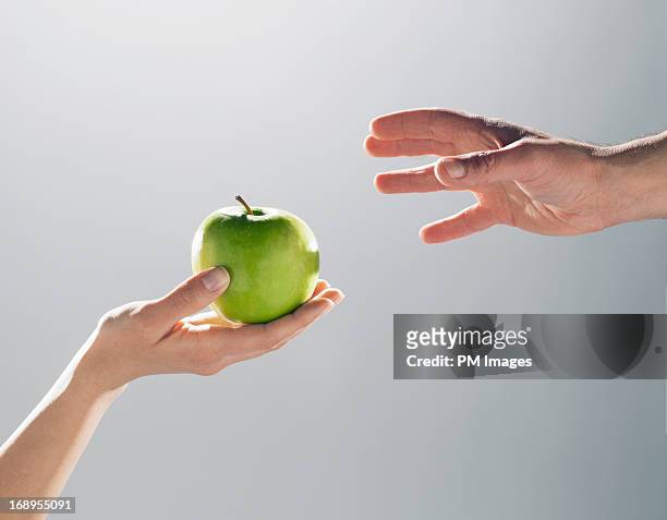 woman handing man an apple - fotografia da studio fotografías e imágenes de stock