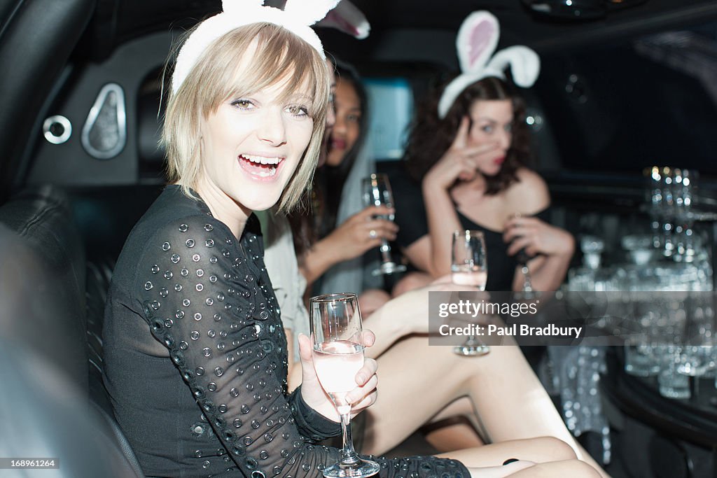 Women in bunny ears having champagne in back of limo