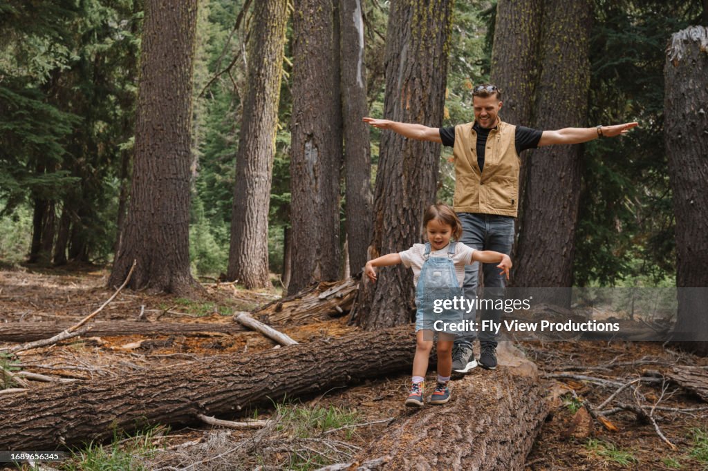 Father and daughter balance on a fallen tree branch