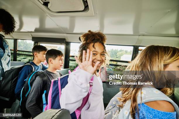 medium shot smiling and waving middle school girl departing school bus - scuolabus foto e immagini stock