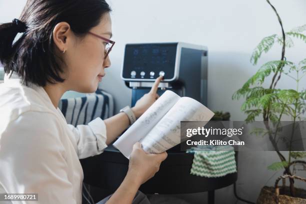 asian woman reading instruction manual for coffee maker - manual fotografías e imágenes de stock