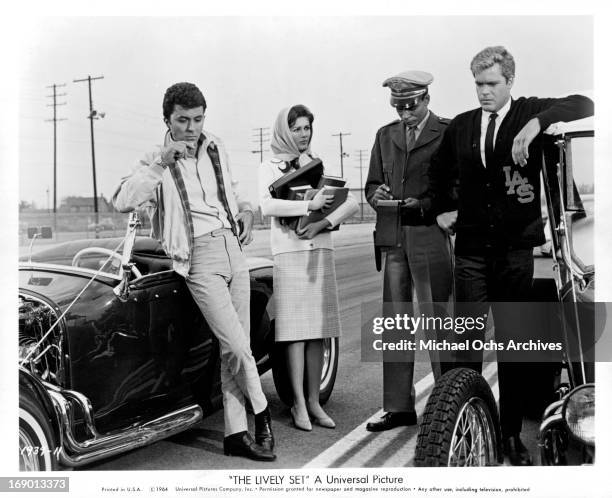 Pamela Tiffin watches as James Darren and Doug McClure receive traffic citations in a scene from the film 'The Lively Set', 1964.