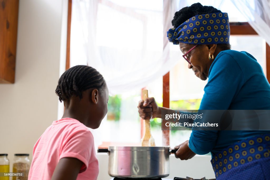 Großmutter rührt Topf Brei mit Enkelin, die zuschaut