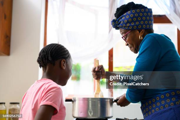 großmutter rührt topf brei mit enkelin, die zuschaut - traditionelle südafrikanische kultur stock-fotos und bilder