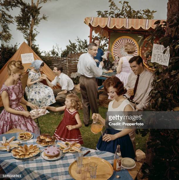 Group of adults and a young girl enjoy a family party in a domestic garden setting, they play games and are served cake, buns, tarts and fruit juice...