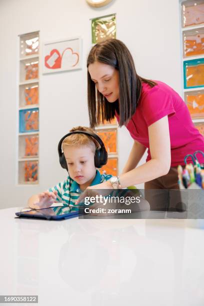 female specialist in speech therapy working with boy wearing headphones and using tablet - learning disability stock pictures, royalty-free photos & images