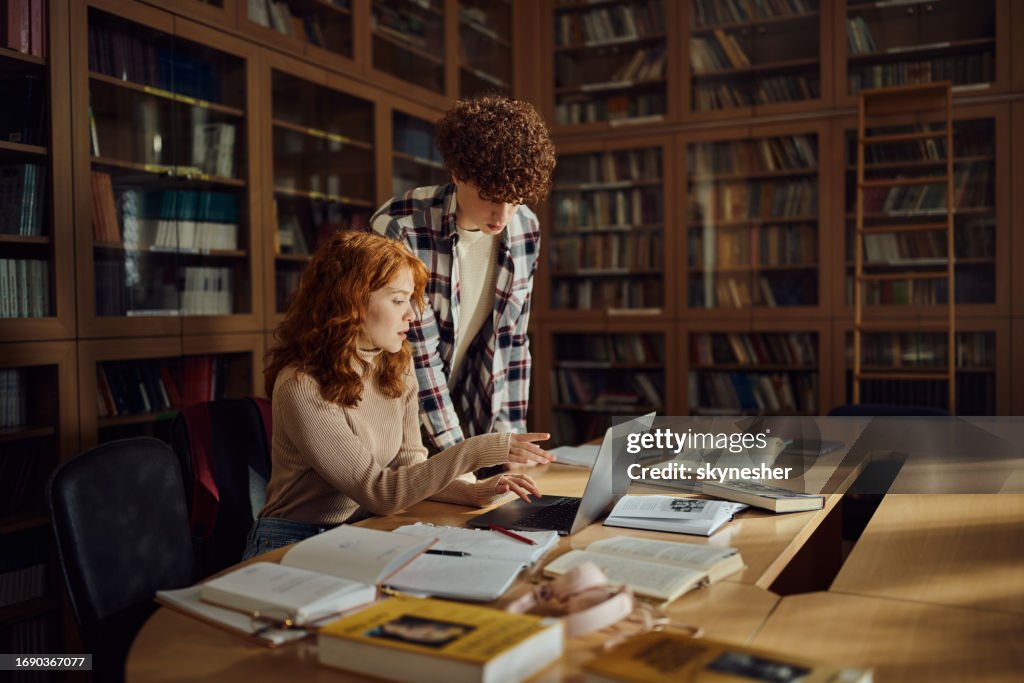 High school students using laptop in library.