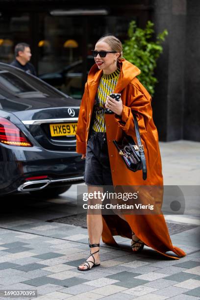 Chloe King wears orange coat, denim shorts, black bag outside Emilia Wickstead during London Fashion Week September 2023 at the on September 18, 2023...
