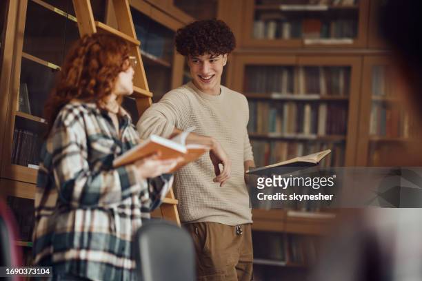 glückliche gymnasiasten unterhalten sich, während sie bücher in der bibliothek lesen. - literatur stock-fotos und bilder