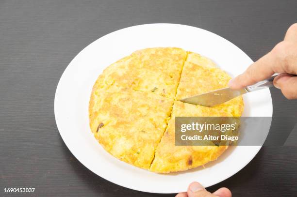 a person cuts a spanish omelette into pieces. - tortilla de patata fotografías e imágenes de stock