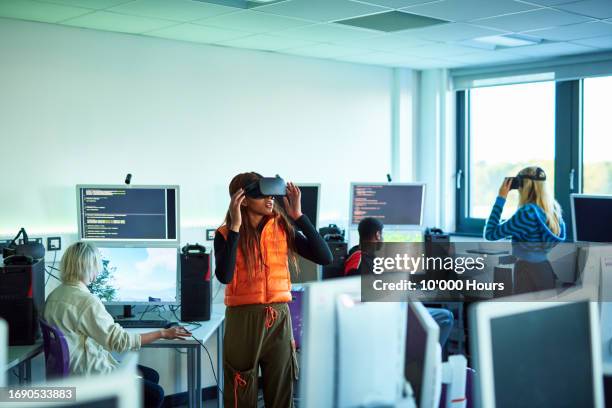 two young women wearing vr headsets in technical college with male classmates sitting at computers - virtual reality classroom stock pictures, royalty-free photos & images