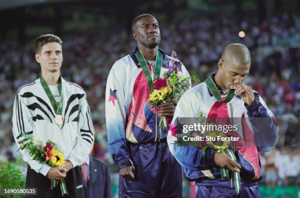 Allen Johnson from the United States stand on the podium for the national anthem alongside compatriot sliver medalist Mark Crear and bronze medalist...