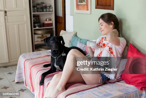 Young woman on the sofa with her dog, having tea Young woman on the sofa with her dog, having tea