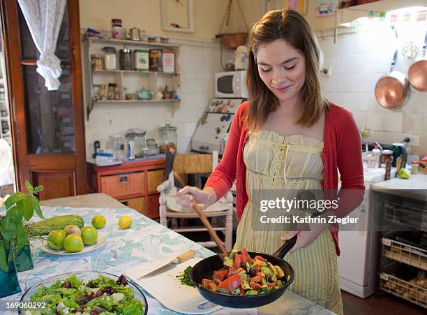 young woman holding a pan with sautéed vegetables - sauteren stockfoto's en -beelden