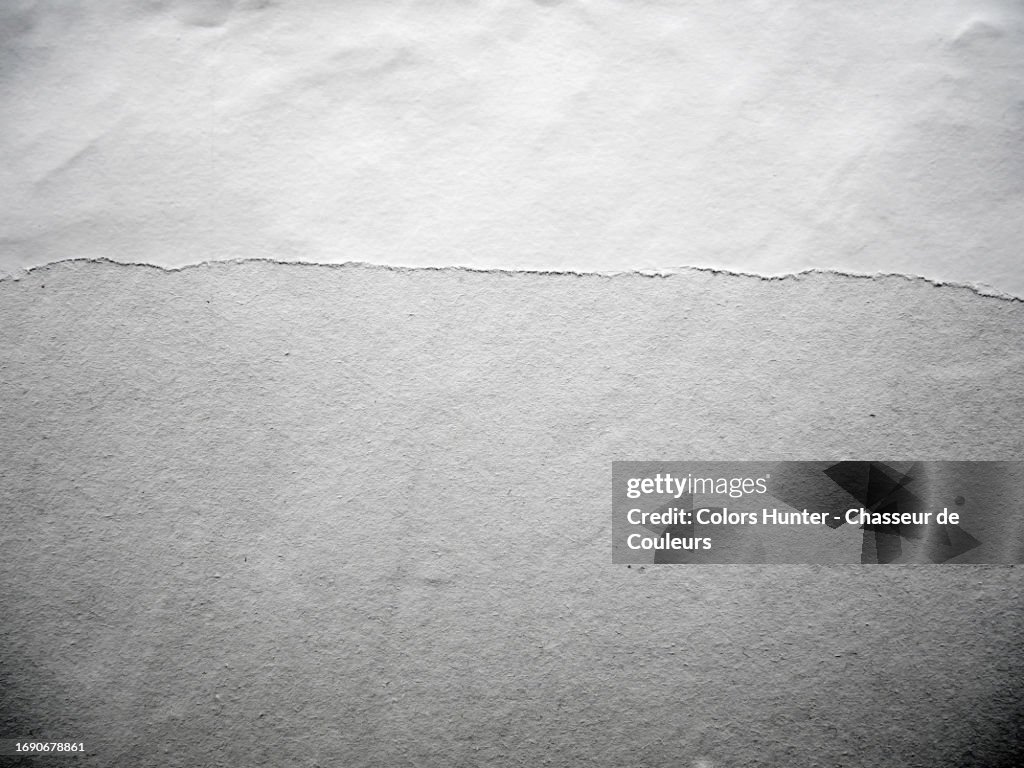 Close-up of white and gray empty paper posters, stuck and torn on a wall with shadows in Paris, France