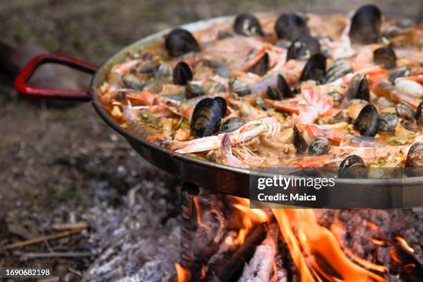 paella mit meeresfrüchten, die über einem holzfeuer gekocht wird - fischmousse stock-fotos und bilder