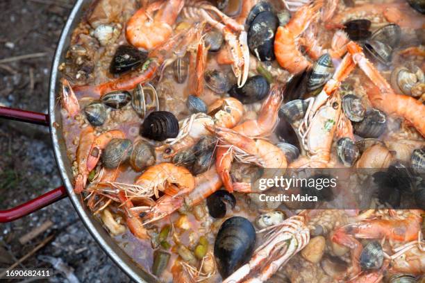 paella mit meeresfrüchten, die über einem holzfeuer gekocht wird - fischmousse stock-fotos und bilder