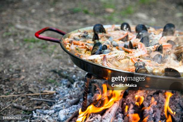 paella mit meeresfrüchten, die über einem holzfeuer gekocht wird - fischmousse stock-fotos und bilder