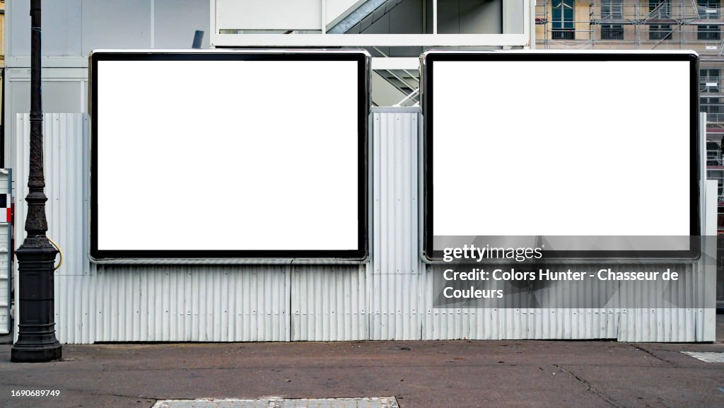 Two empty white advertising panels on a white corrugated iron wall with an asphalt street and a retro-style street light in Paris, France