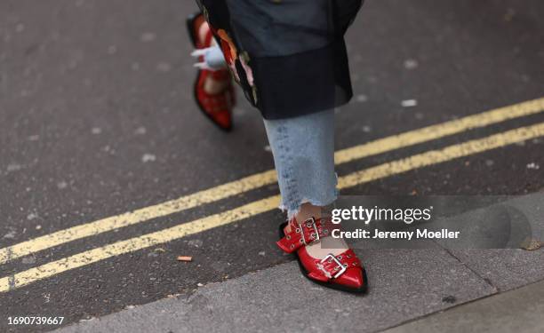 Fashion Week Guest was seen wearing red leather shoes, a denim jeans, abbeige bag, dark shades, a black top under a black transparent dress with...