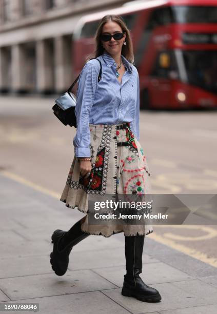 Fashion Week Guest was seen wearing black leather boots along with a black bag, dark shades, a white and blue striped Polo Ralph Lauren shirt with...