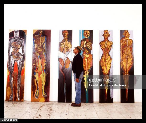 Portrait of American artist Emilio Cruz as he poses with six panels from one of his 'Homo Sapiens' series of paintings, 2000s.
