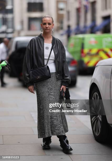 Fashion week guest was seen wearing black leather boots, a grey skirt, a white Loewe top, a black leather jacket as well as silver earrings and a...