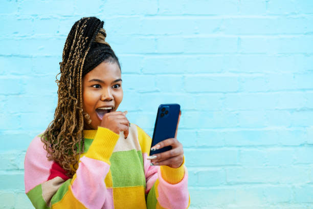 woman reacting to smart phone - black woman phone shock stock pictures, royalty-free photos & images