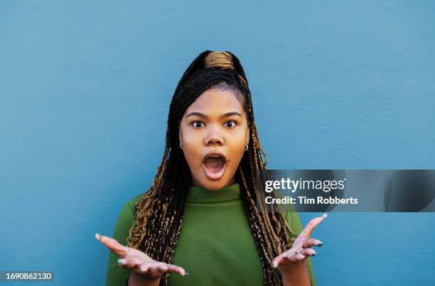 woman looking surprised in front of blue wall - euforia foto e immagini stock