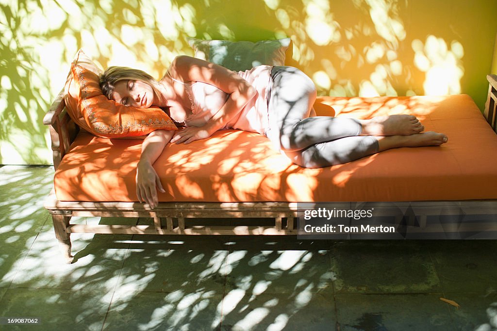 Woman sleeping on sunny patio bench