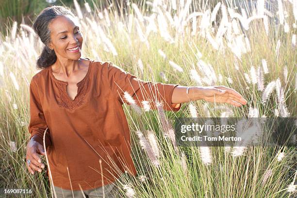 woman walking in sunny field - mature woman beauty arm stockfoto's en -beelden