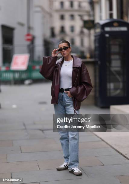 Fashion week guest was seen wearing black and white adidas samba sneaker, a denim jeans, a black belt, a white top with a yellow gold chain, dark...